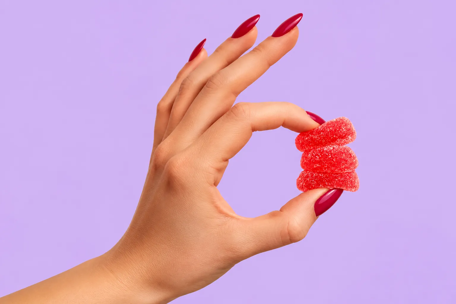 Mano sosteniendo gomitas rojas sobre un fondo lila